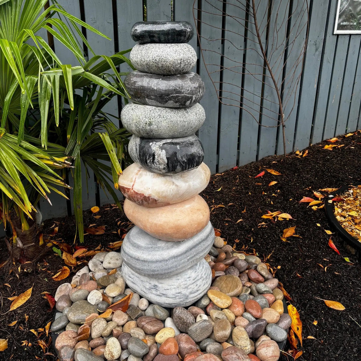 Mid Ulster Garden Centre cascading marble pebble fountain featuring stacked grey and warm-toned boulders in a garden.